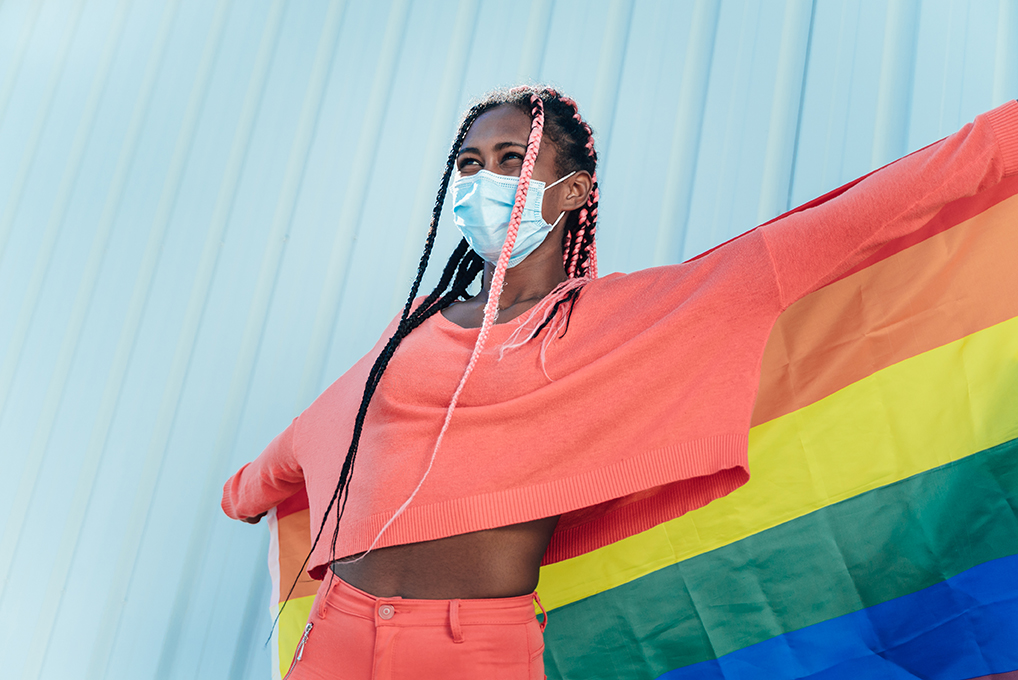 Young black gay woman with face mask holding a lgbt gay pride rainbow flag