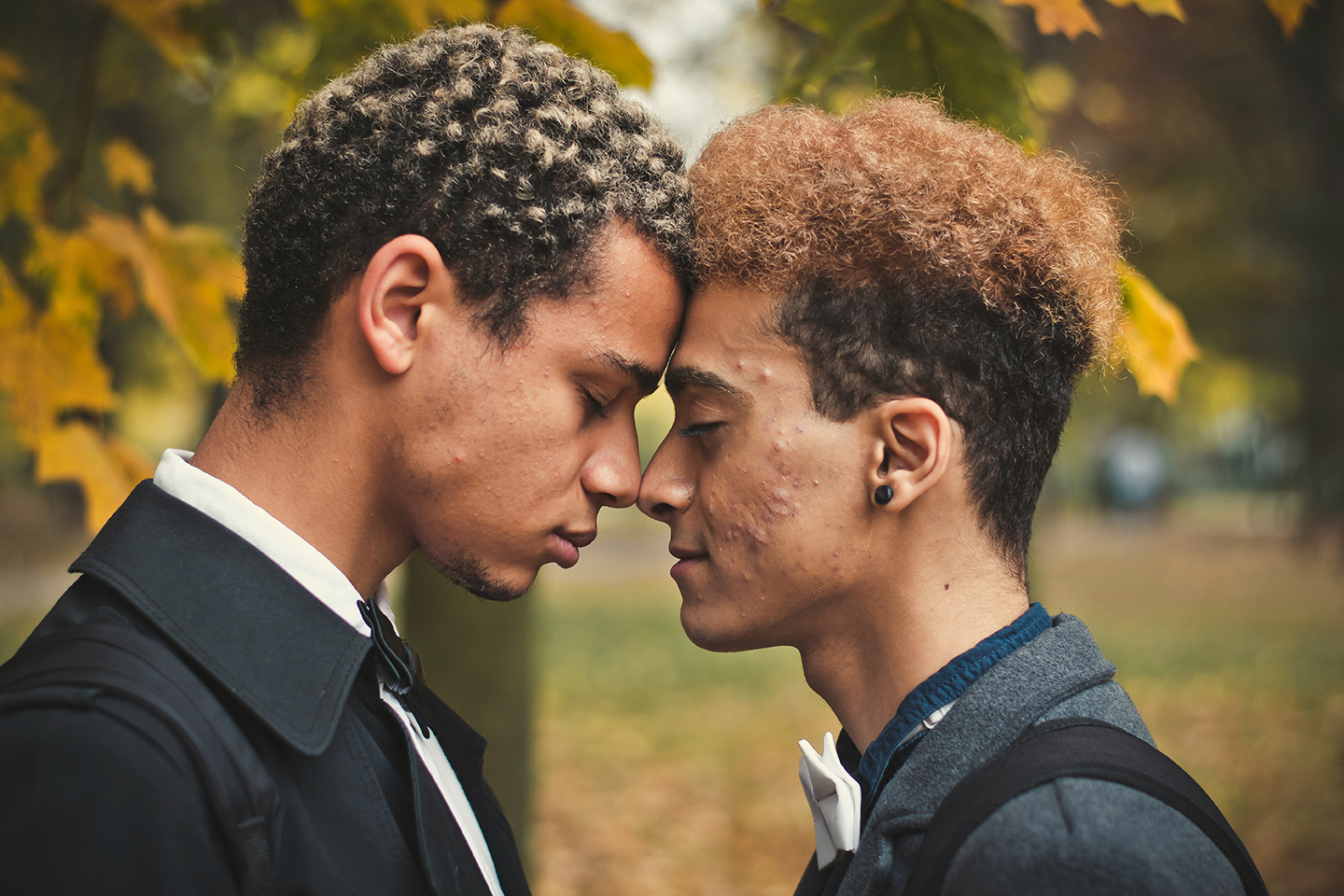 Handsome young gay couple standing head to head in park.